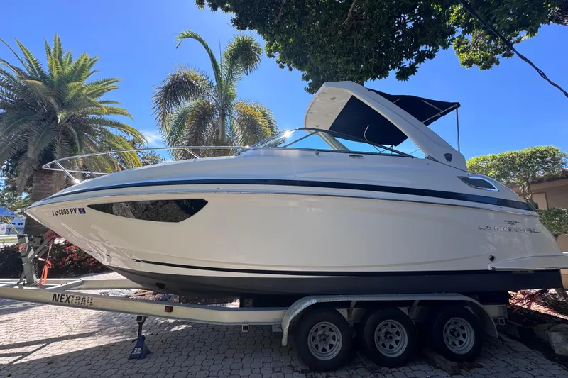 Slide: The Image of 2015 Regal 28 Express boat on trailer, surrounded by palm trees under clear blue sky. - 3