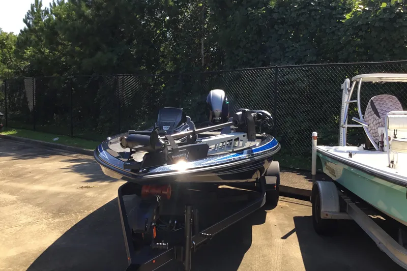 Slide: The Image of 2024 Skeeter ZX 150 boat on trailer, parked outdoors near trees and fence. - 2