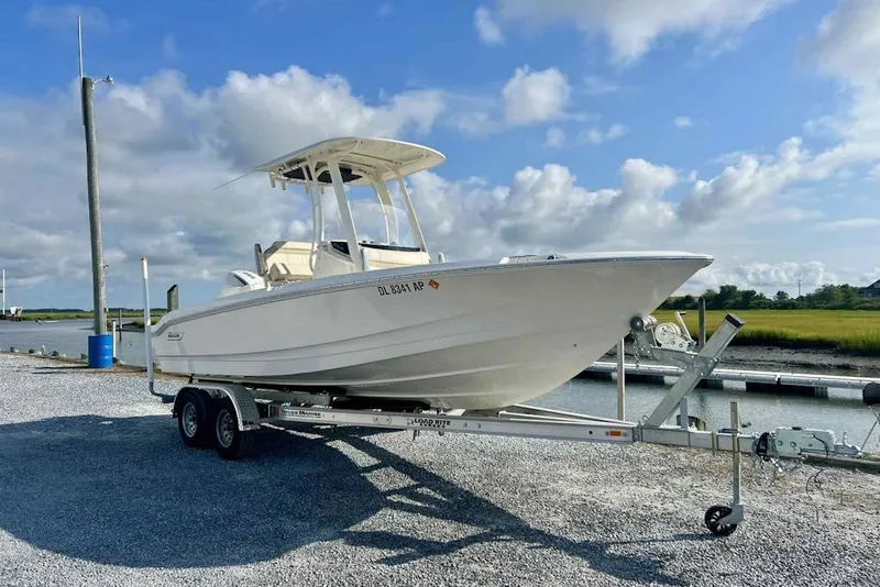 Slide: The Image of 2024 Boston Whaler 220 Dauntless boat on trailer, parked near a marina under a blue sky. - 0
