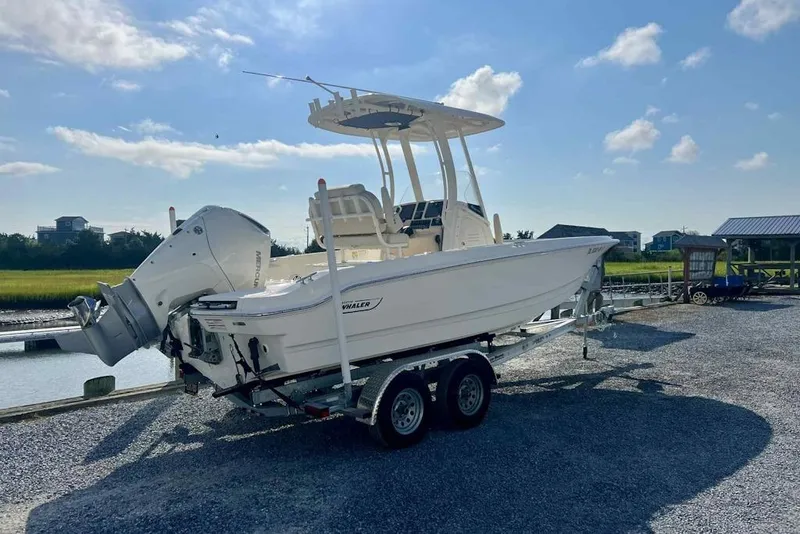 Slide: The Image of 2024 Boston Whaler 220 Dauntless boat on trailer by waterfront under blue sky. - 1