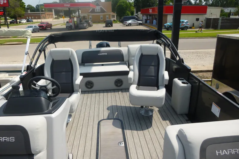 Slide: The Image of 2025 Harris boat interior with modern seating and steering, parked near a gas station. - 4