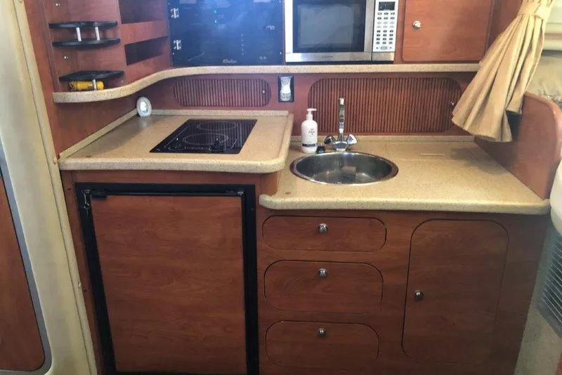 Slide: The Image of 2006 Rinker 342 Express Cruiser kitchen with stove, sink, microwave, and wooden cabinetry. - 22