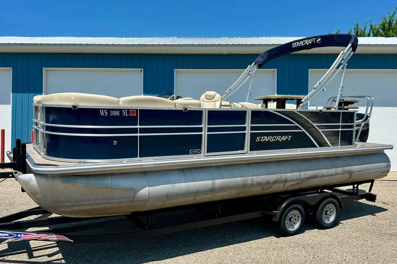 Slide: The Image of 2017 Starcraft CX 23 RE pontoon boat on trailer, parked outside blue building. - 1