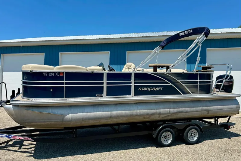 Slide: The Image of 2017 Starcraft CX 23 RE pontoon boat on trailer, blue exterior, parked by blue building. - 31