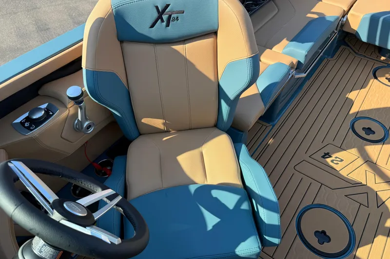 Slide: The Image of 2025 MasterCraft XT24 boat interior with tan and blue seating, steering wheel, and control panel. - 19