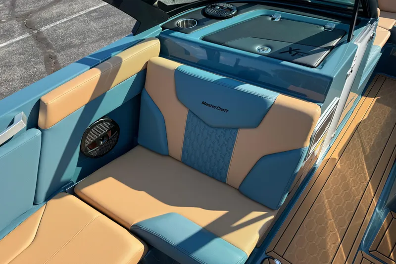 Slide: The Image of 2025 MasterCraft XT24 boat interior with blue and tan seating, speaker, and storage compartment. - 26