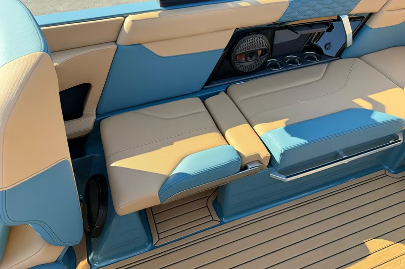 Slide: The Image of 2025 MasterCraft XT24 boat interior with tan and blue seating, cup holders, and speaker system. - 32