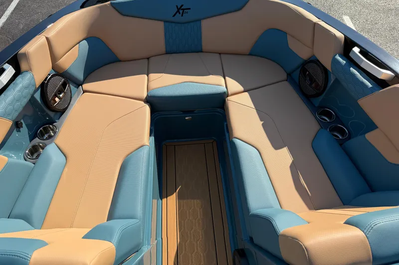 Slide: The Image of 2025 MasterCraft XT24 boat interior with tan and blue seating, cup holders, and speakers. - 37