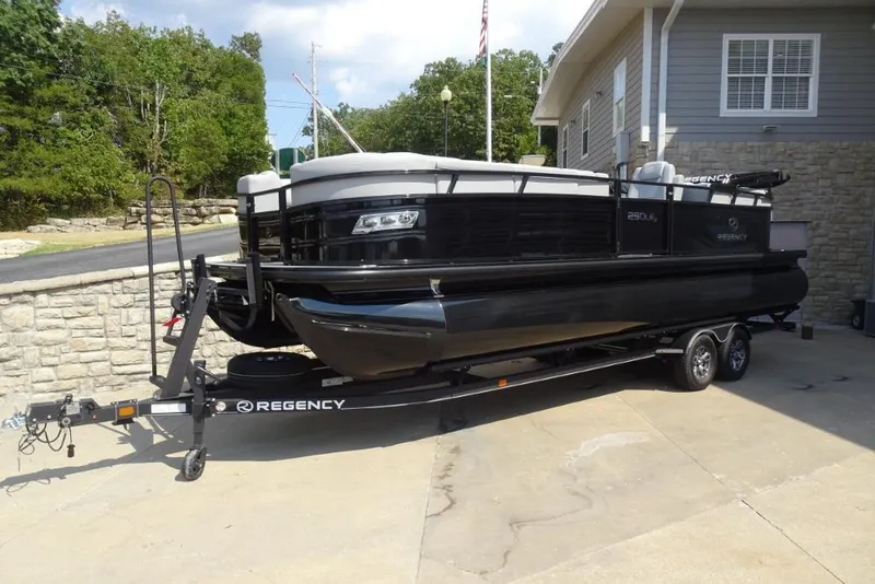 Slide: The Image of 2024 Regency 250 LE3 pontoon boat on trailer, parked near a building. - 24