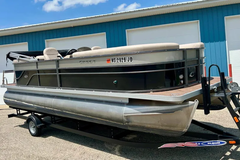The Image of 2014 Crest 230 Crest II SLC pontoon boat on trailer, parked near blue building. - 1