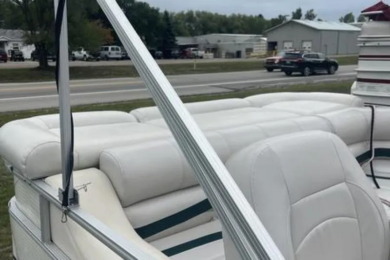 Slide: The Image of 1999 Bennington Twin-Toon boat with white cushioned seating, parked near a road. - 13