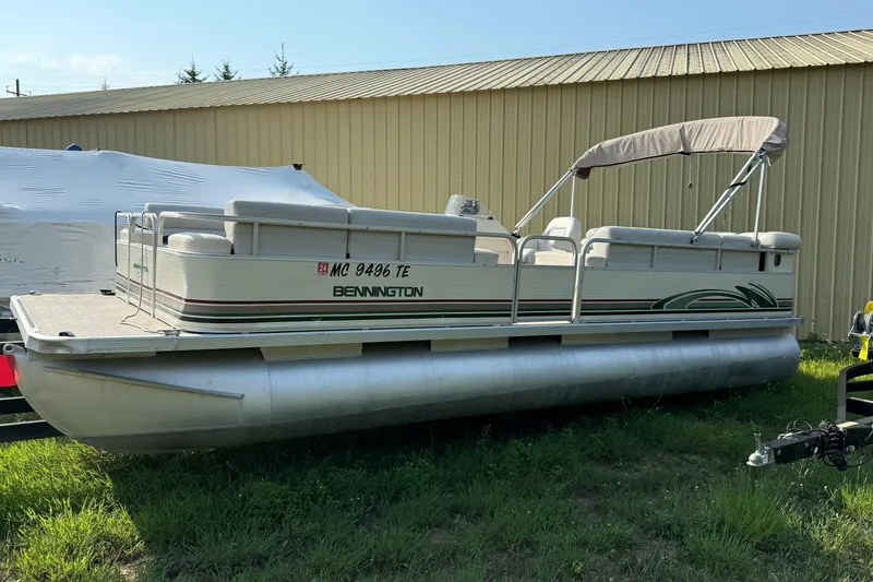 Slide: The Image of 1999 Bennington Twin-Toon pontoon boat with canopy, parked on grass beside a building. - 2