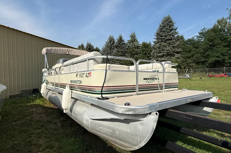 Slide: The Image of 1999 Bennington twin-toon pontoon boat on trailer, parked near a building and trees. - 5