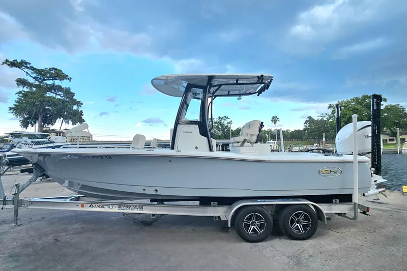 Slide: The Image of 2023 Sea Hunt BX 25 FS boat on trailer, parked near water under a cloudy sky. - 1
