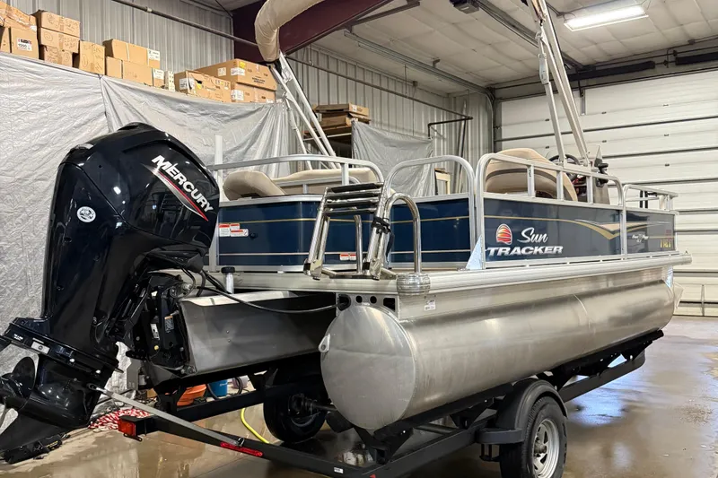 Slide: The Image of 2023 Sun Tracker Bass Buggy 18 DLX pontoon boat with Mercury outboard motor in a garage. - 2