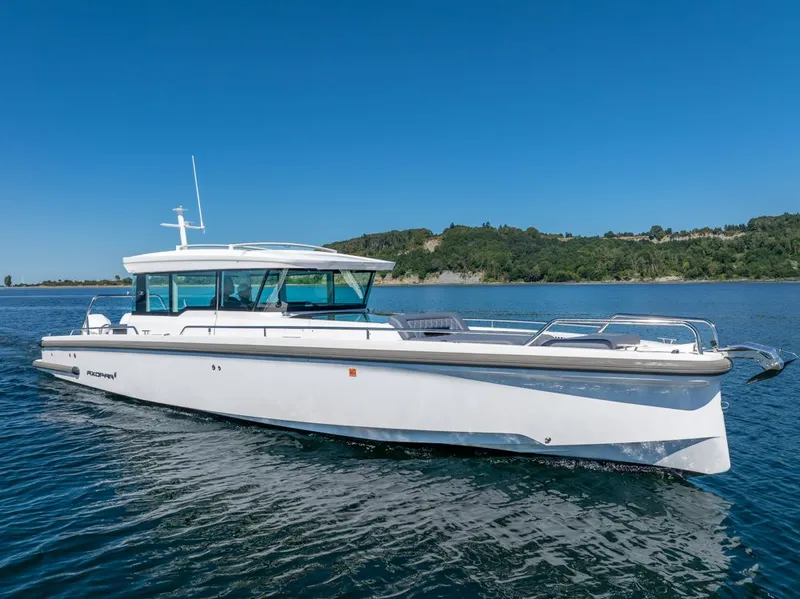 Slide: The Image of 2021 Axopar Cross Cabin boat cruising on a clear blue lake with scenic shoreline. - 45