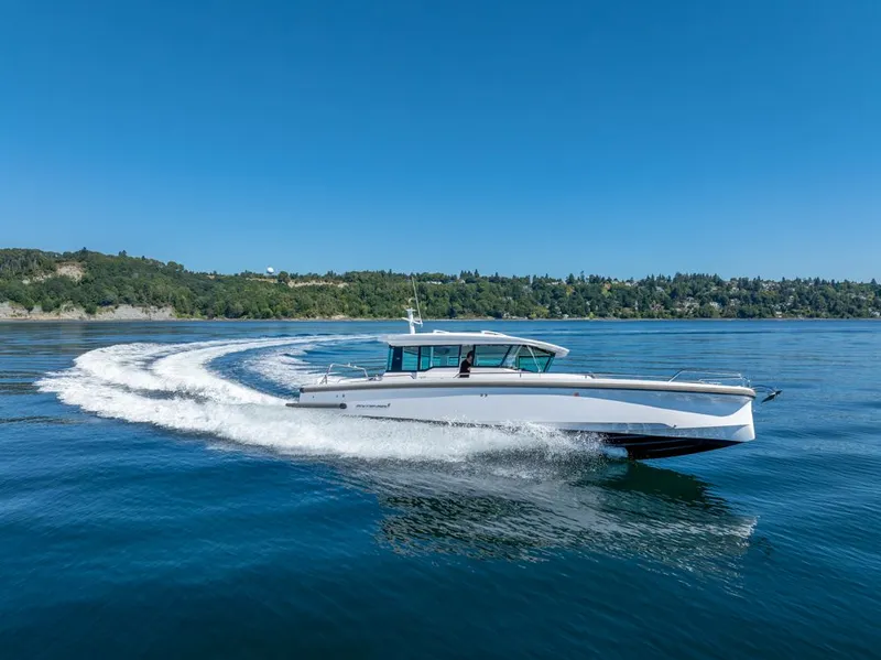 Slide: The Image of 2021 Axopar Cross Cabin boat cruising on a clear blue lake with scenic shoreline. - 48