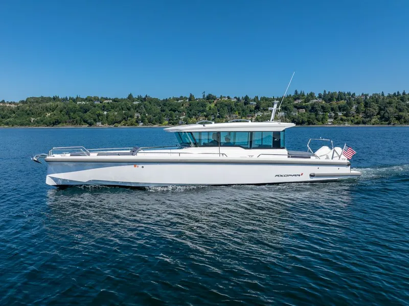 Slide: The Image of 2021 Axopar Cross Cabin boat cruising on a serene lake under a clear blue sky. - 5