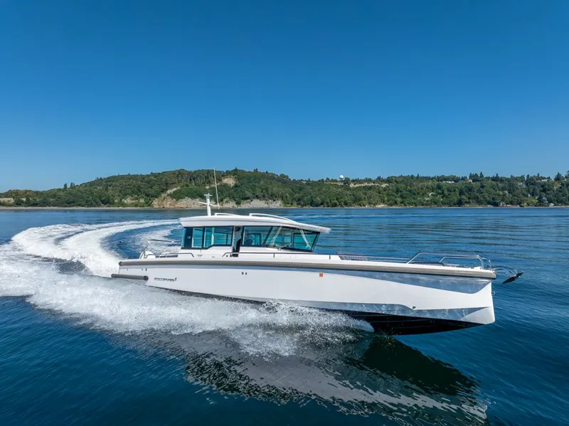 Slide: The Image of 2021 Axopar Cross Cabin boat cruising on clear blue water with scenic green shoreline. - 6