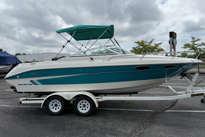 Slide: The Image of 1995 Sea Ray 220 Cuddy Cabin boat on trailer, teal and white design, parked outdoors. - 3
