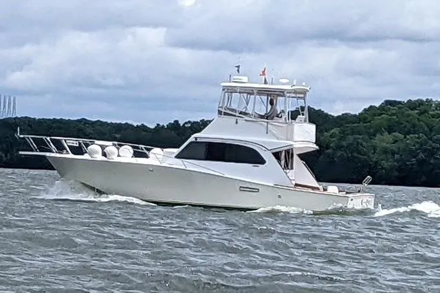 The Image of 1984 Post 43 Sport Fisherman boat cruising on a lake with lush green shoreline. - 1