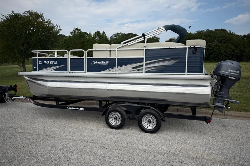 Slide: The Image of 2018 Sweetwater Sunrise 206 F pontoon boat on trailer, parked near a lake under blue sky. - 9