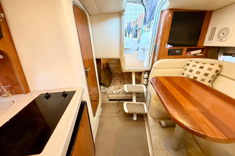 Slide: The Image of 2004 Four Winns 298 Vista cabin interior with kitchenette, seating, and wooden table. - 28