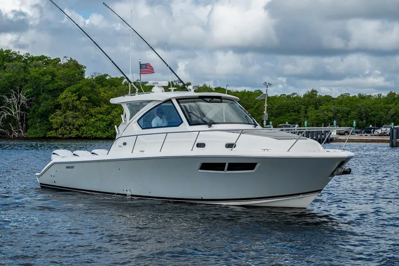 Slide: The Image of 2022 Pursuit OS 355 Offshore boat cruising on a calm waterway with lush greenery. - 5