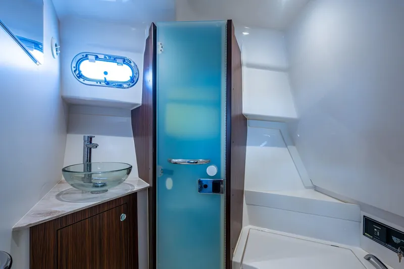 Slide: The Image of 2022 Pursuit OS 355 Offshore bathroom with glass sink, storage shelves, and porthole window. - 55