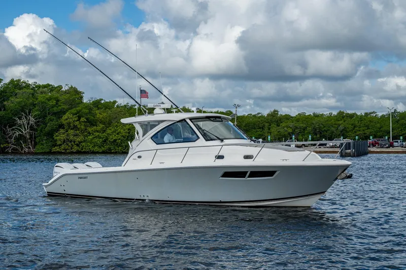 Slide: The Image of 2022 Pursuit OS 355 Offshore boat cruising on a calm waterway with lush greenery. - 6