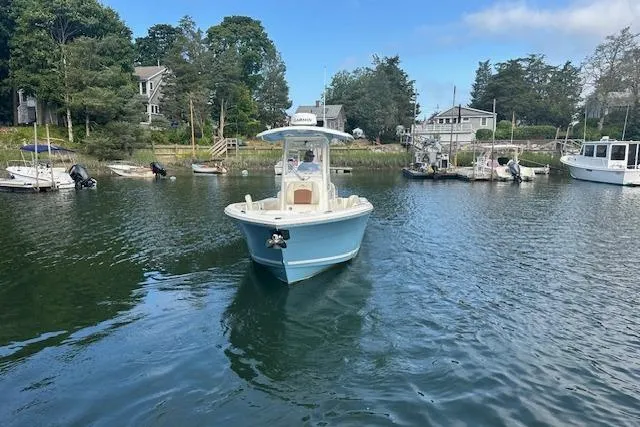 Slide: The Image of 2023 Cobia 240 Center Console boat on a serene lake with surrounding trees and houses. - 2