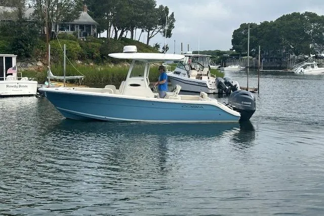 Slide: The Image of 2023 Cobia 240 Center Console boat on calm water near a dock, with trees in the background. - 5