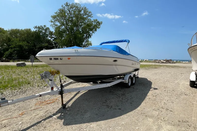 Slide: The Image of Four Winns boat on trailer with blue cover, parked near a beach under clear sky. - 3