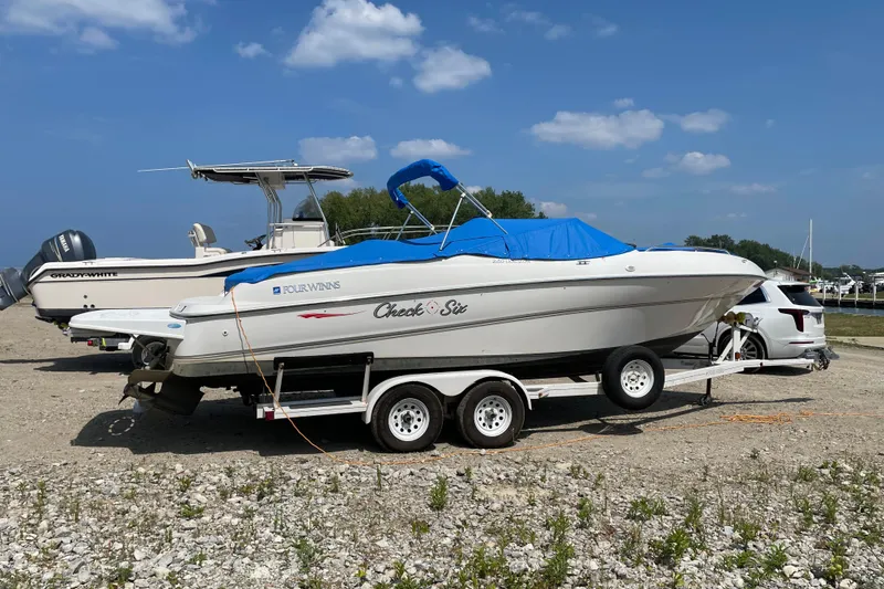 Slide: The Image of Four Winns boat on trailer with blue cover, parked beside a vehicle under a clear sky. - 5