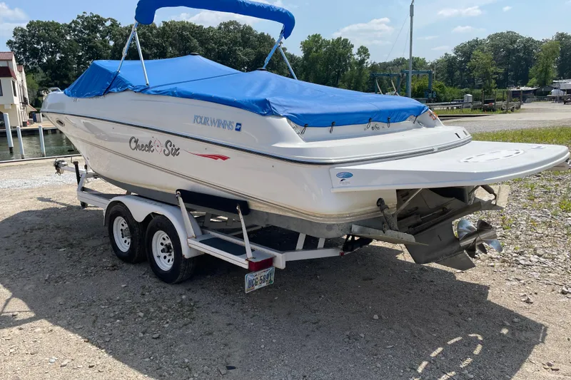 Slide: The Image of Four Winns boat with blue cover on trailer, parked outdoors on a sunny day. - 6