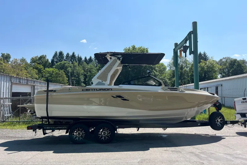 The Image of 2025 Centurion Ri230 boat on trailer, parked outdoors under clear sky. - 0