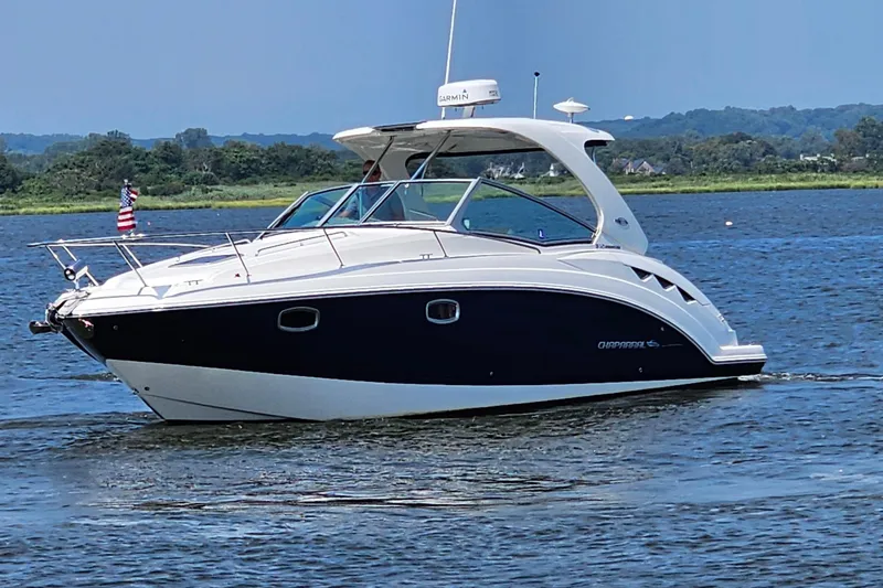 Slide: The Image of 2015 Chaparral 310 Signature boat cruising on a scenic lake with lush green shoreline. - 3