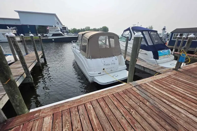 Slide: The Image of 2002 Sea Ray 260 Sundancer docked at marina, featuring tan canopy and wooden pier. - 13