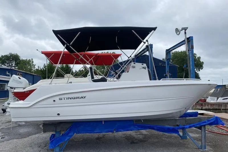 The Image of 2025 Stingray 173CC boat with black canopy on a lift, overcast sky. - 1