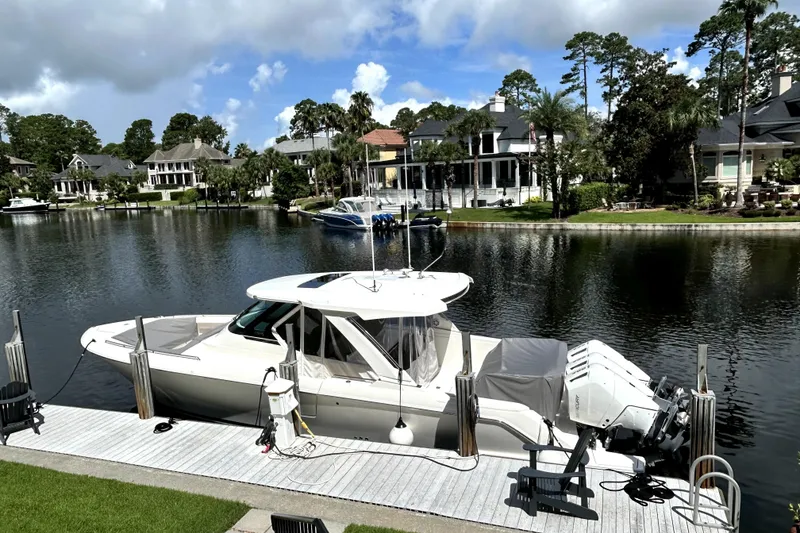 Slide: The Image of 2023 Tiara Yachts 38 LS docked by waterfront homes under a partly cloudy sky. - 1