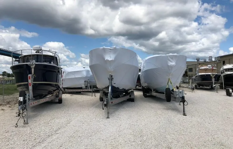 The Image of 2025 Cutwater C-32 Sedan boats on trailers, covered, under cloudy sky. - 0