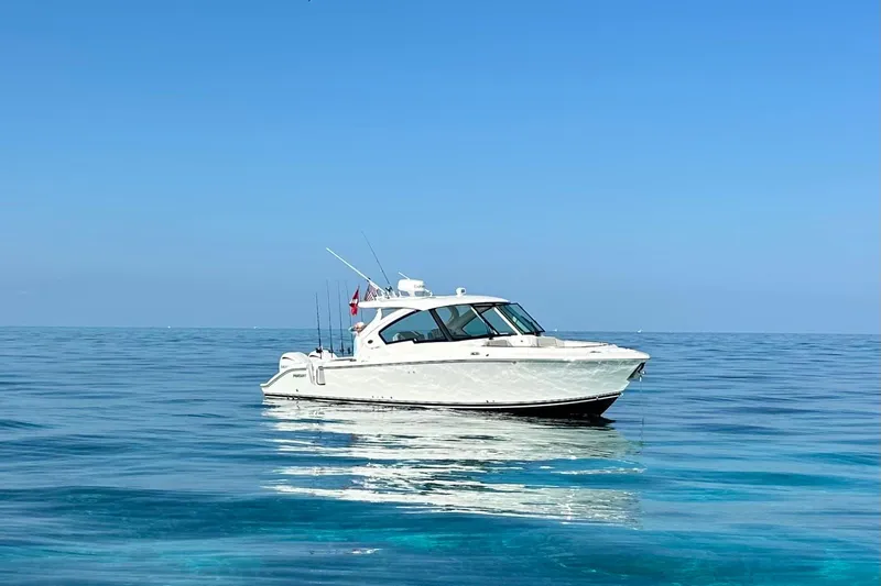 Slide: The Image of 2023 Pursuit DC 326 Dual Console boat cruising on calm water at sunset. - 0