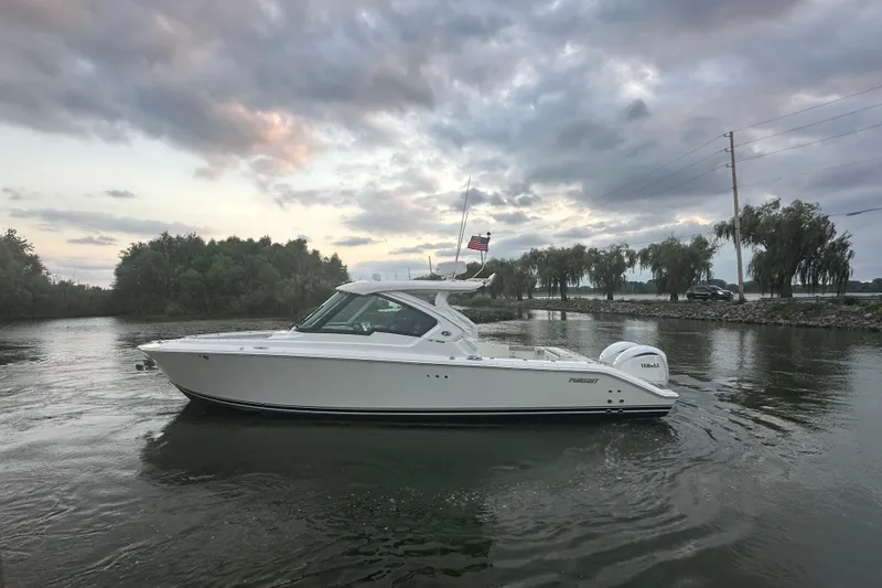Slide: The Image of 2023 Pursuit DC 326 Dual Console boat interior with twin engines, docked on calm water. - 27