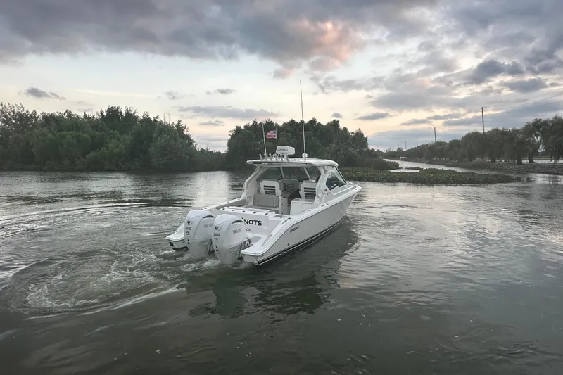 Slide: The Image of 2023 Pursuit DC 326 Dual Console boat docked by a serene river under cloudy skies. - 29