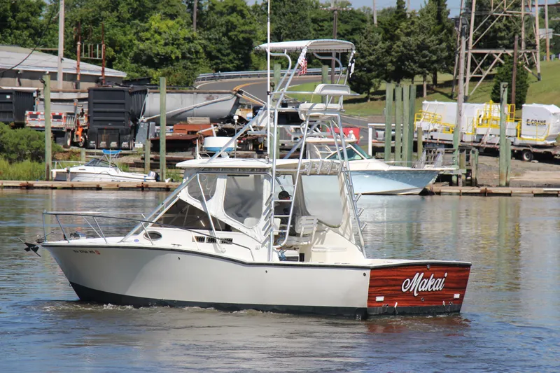 Slide: The Image of 2004 Carolina Classic 28 boat named "Makai" cruising in a marina with industrial backdrop. - 28