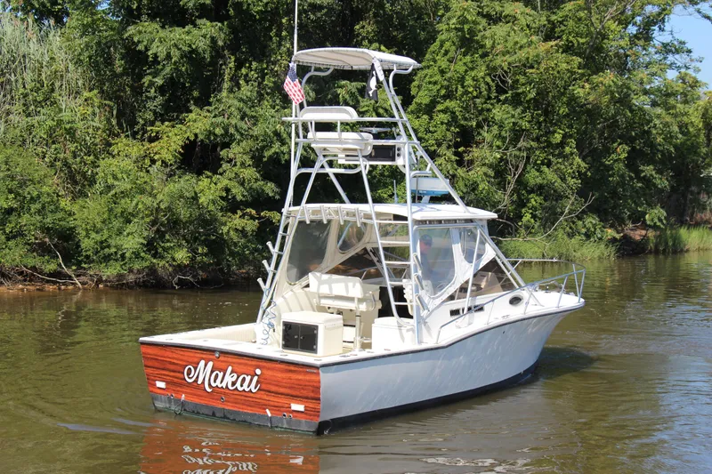 Slide: The Image of 2004 Carolina Classic 28 boat named "Makai" on a calm river, surrounded by lush greenery. - 58