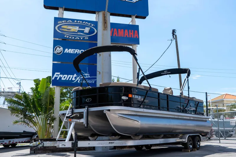 Slide: The Image of 2022 Veranda Relax VR25RC pontoon boat on trailer at dealership, surrounded by signage. - 4