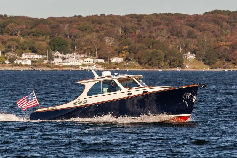 Slide: The Image of 2023 Hinckley Picnic Boat 34 S cruising on a scenic lake with American flag. - 1
