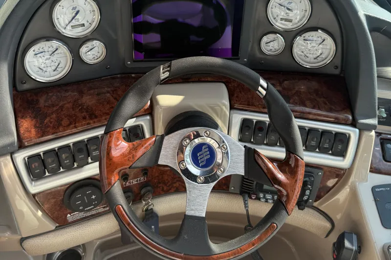 Slide: The Image of Steering wheel and dashboard of 2006 Four Winns 318 Vista boat, featuring wood accents and gauges. - 20