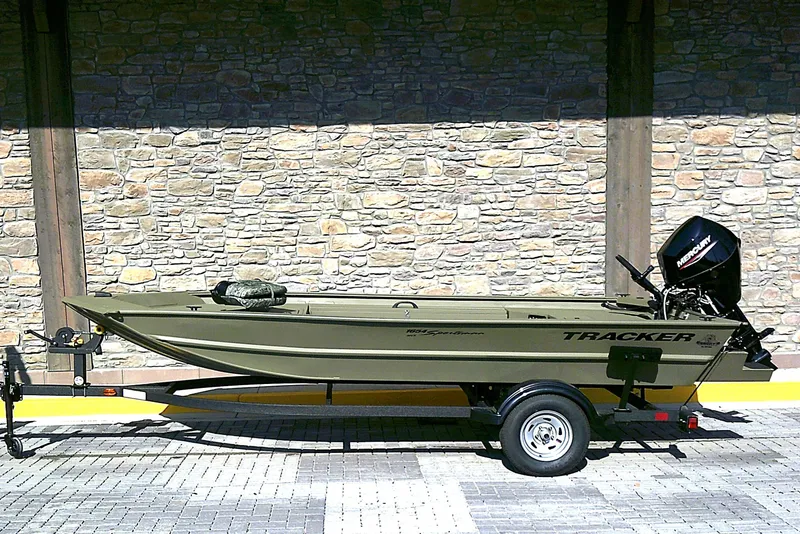 The Image of 2026 Tracker Grizzly 1654 T Sportsman boat on trailer, parked against stone wall. - 0